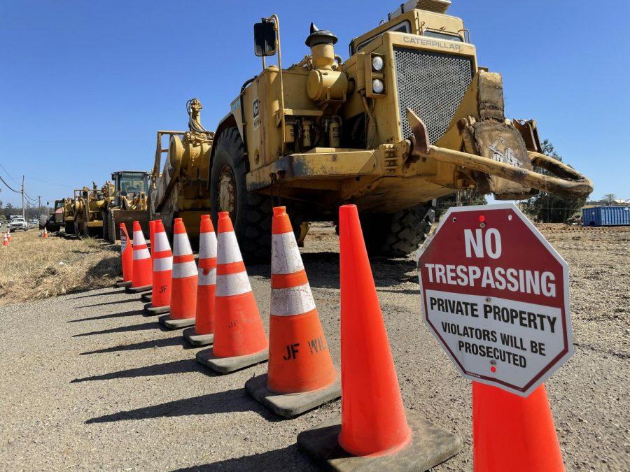 Heavy machinery sits parked behind construction cones and trespassing warnings