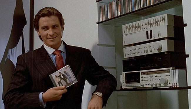 Christian Bale, portraying homicidal investment banker Patrick Bateman, grins while holding a CD (image courtesy of Lions Gate Films.)