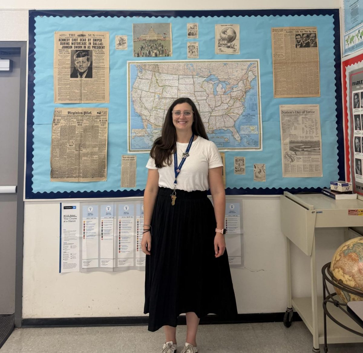 Kelli Peters next to her history board for AP United States History dual enrollment in room 306. 
