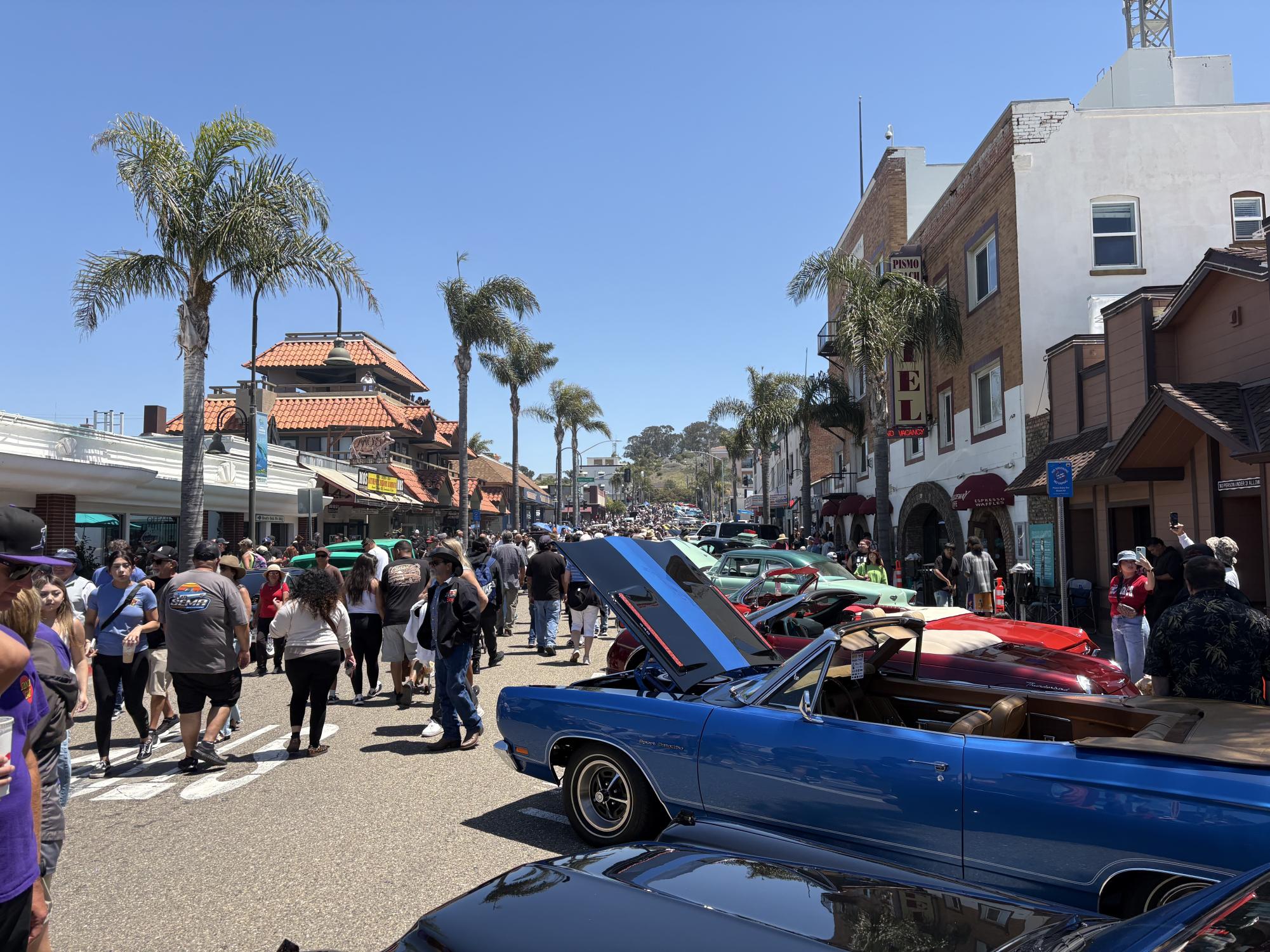 A huge crowd of people all admiring the classic cars parked along the street.
